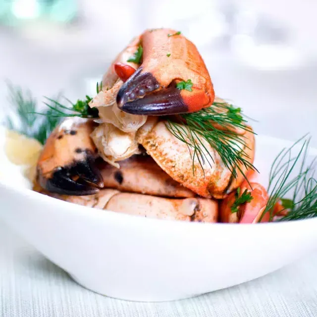 Crab legs are stacked in a white bowl and sprinkled with fresh dill.